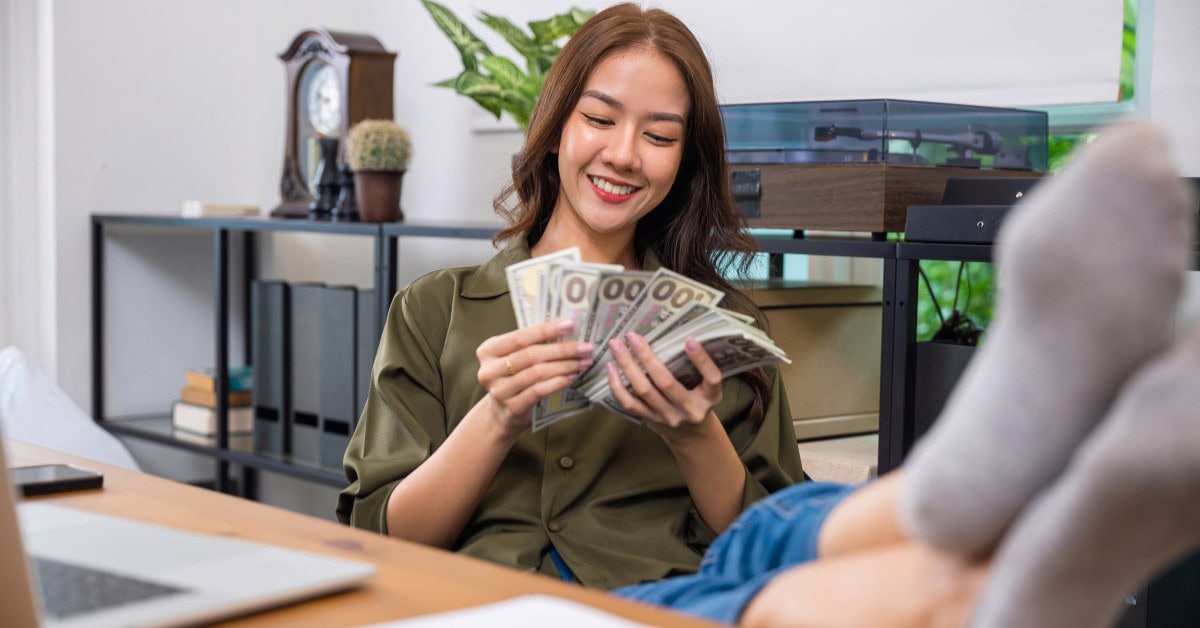 woman reclined in chair holding money - passive income ideas to make 6 figures