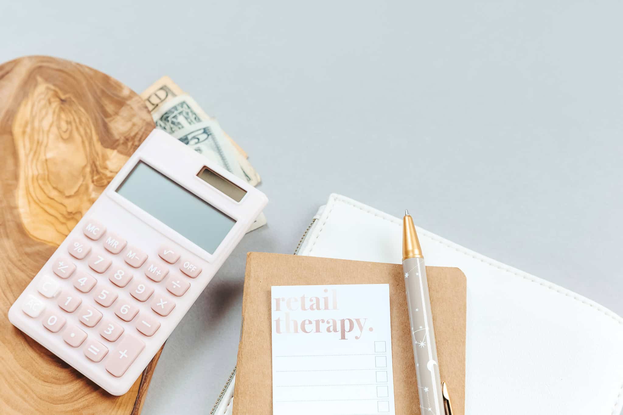 retail-therapy-notepad-pen-money-dollars-calculator-wood-grey-background